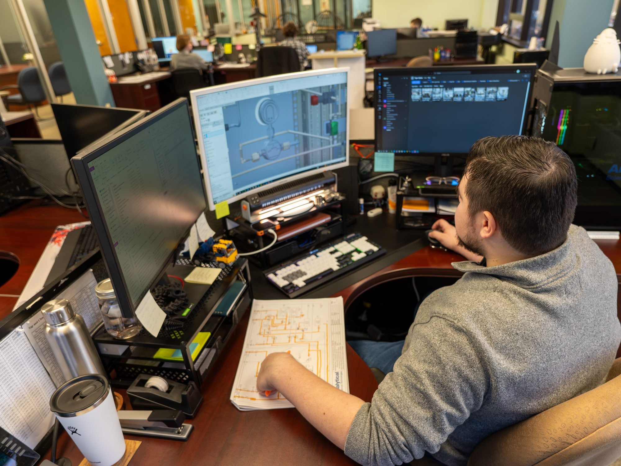 ASTG designer working on a 3D CAD model of an analytical system component at a multi-monitor workstation